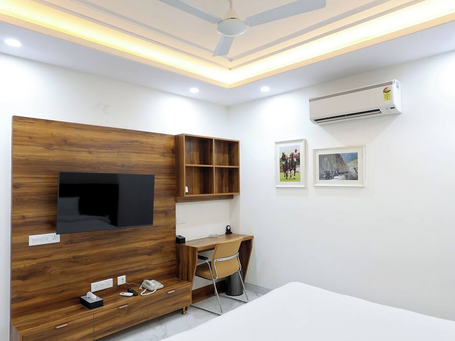 A bedroom with a bed, a TV mounted on a wooden wall, a desk with a chair, and an air conditioning unit on the wall.