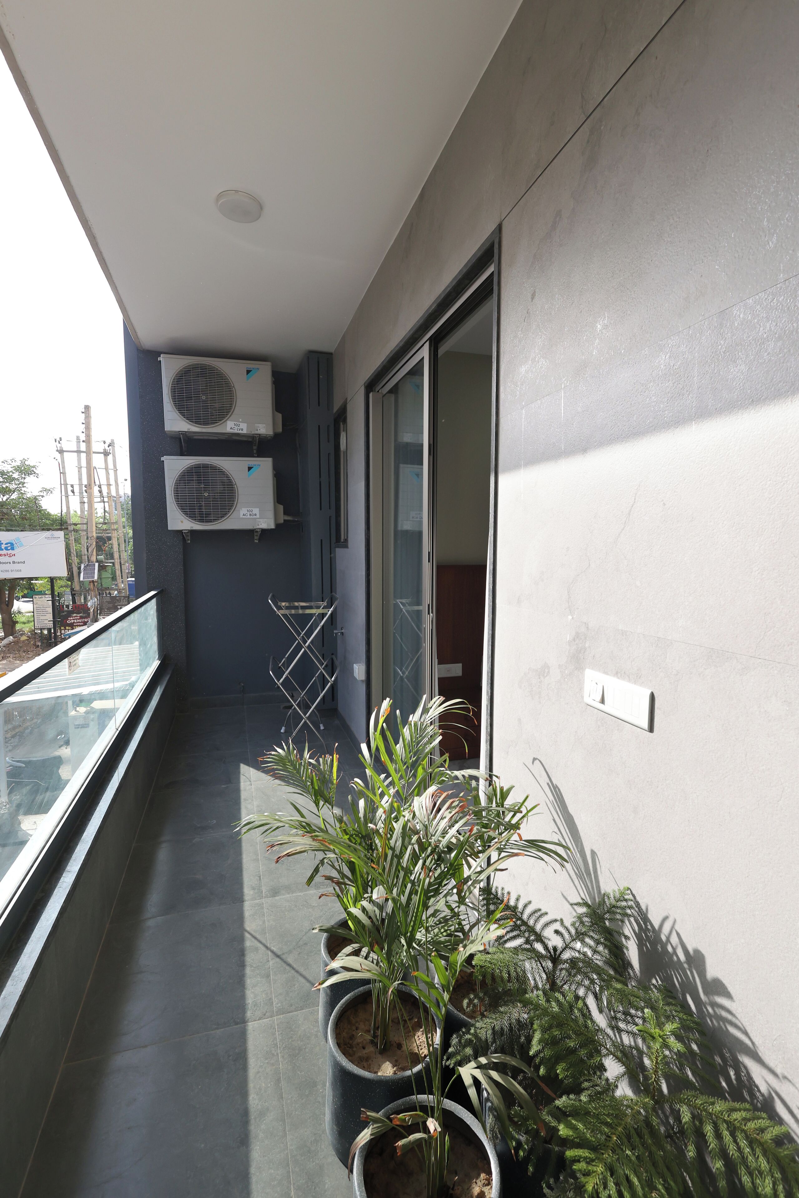 Un balcón con plantas en macetas, unidades de aire acondicionado y una puerta corrediza de vidrio.