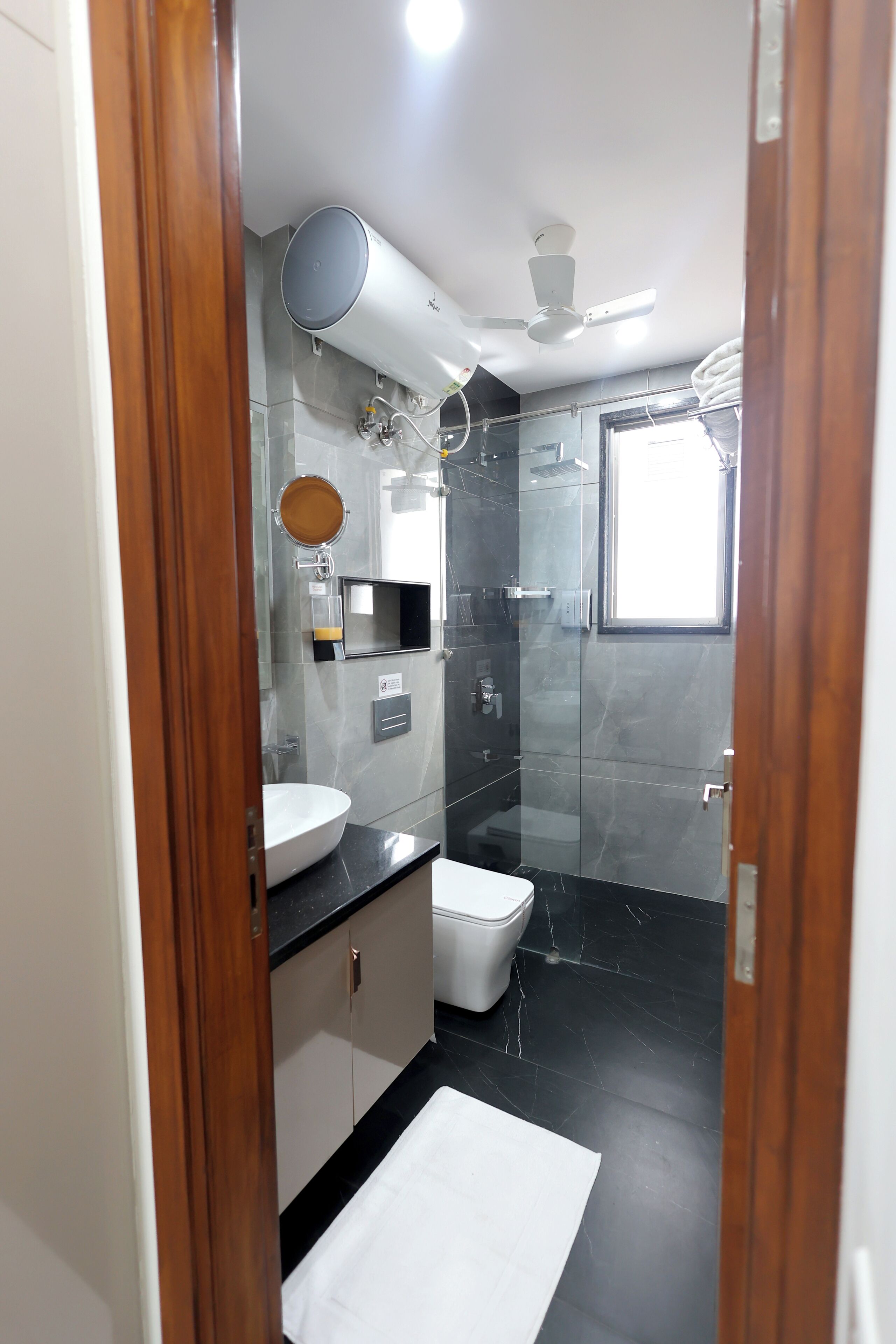 Un baño moderno con cabina de ducha de vidrio, un lavamanos blanco y un ventilador de techo.