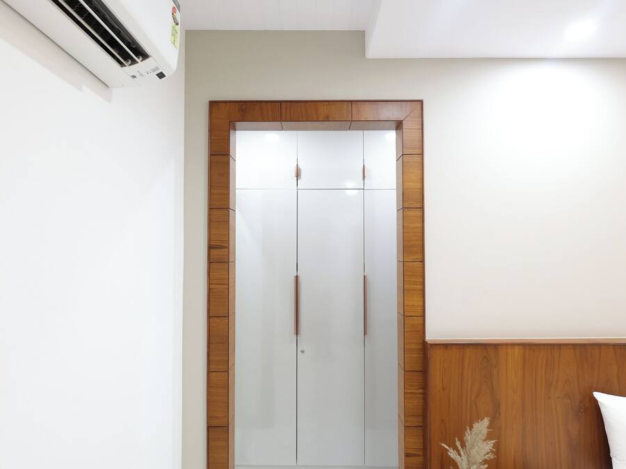 Un dormitorio moderno con un armario de madera, una mesita de noche con un florero y una cama con ropa de cama blanca.