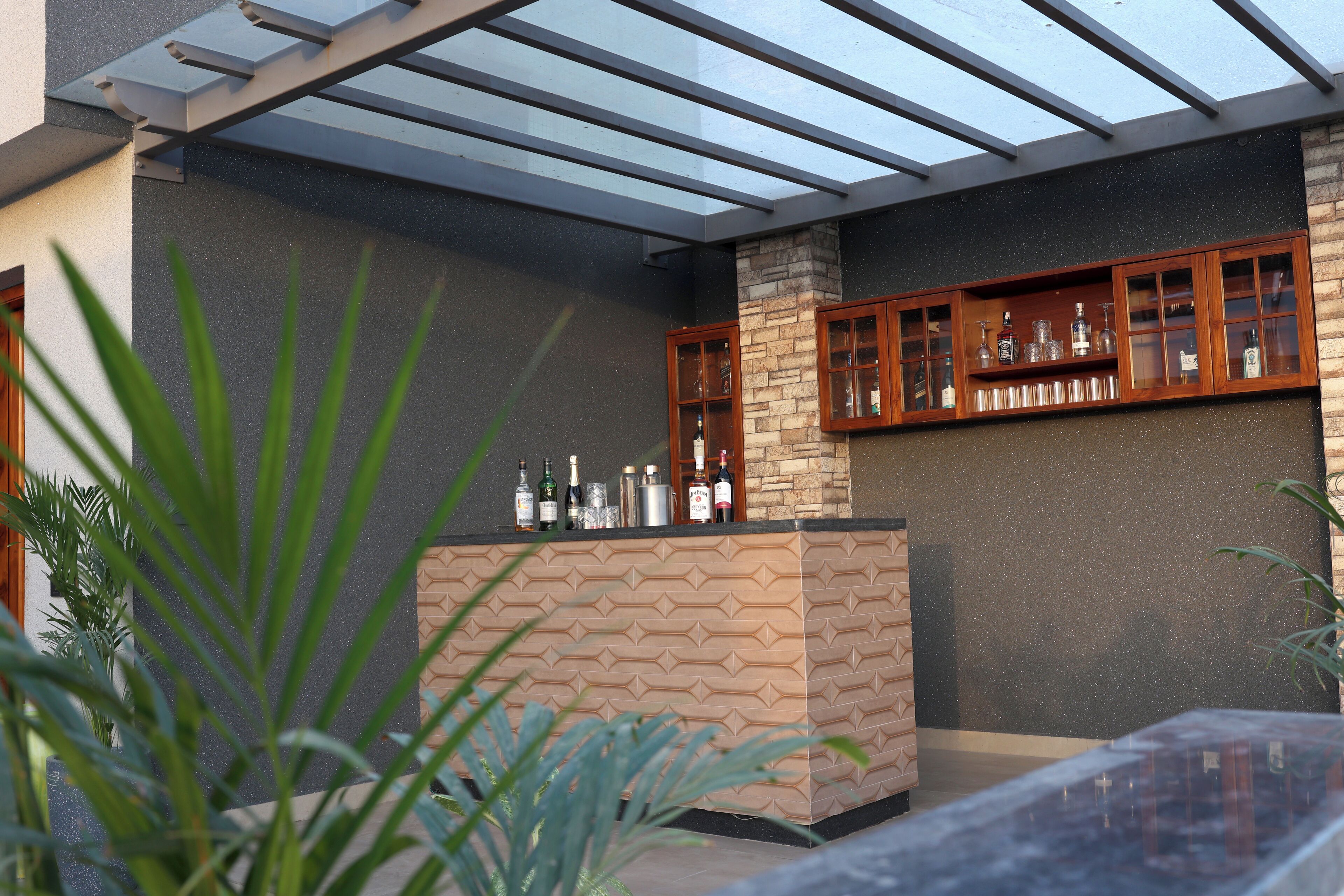 A modern outdoor bar area with a stone pillar, wooden cabinets, and a glass ceiling.