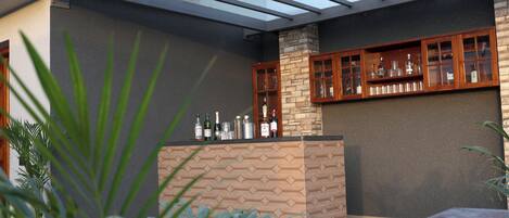 Un espace bar extérieur moderne, doté d’un pilier en pierre, de meubles de rangement en bois et d’un plafond en verre.