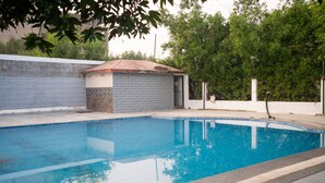 A swimming pool with a tiled deck, a small building with a tiled roof, and a white wall.