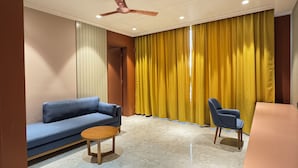 A living room with a blue sofa, a wooden coffee table, a ceiling fan, and yellow curtains.