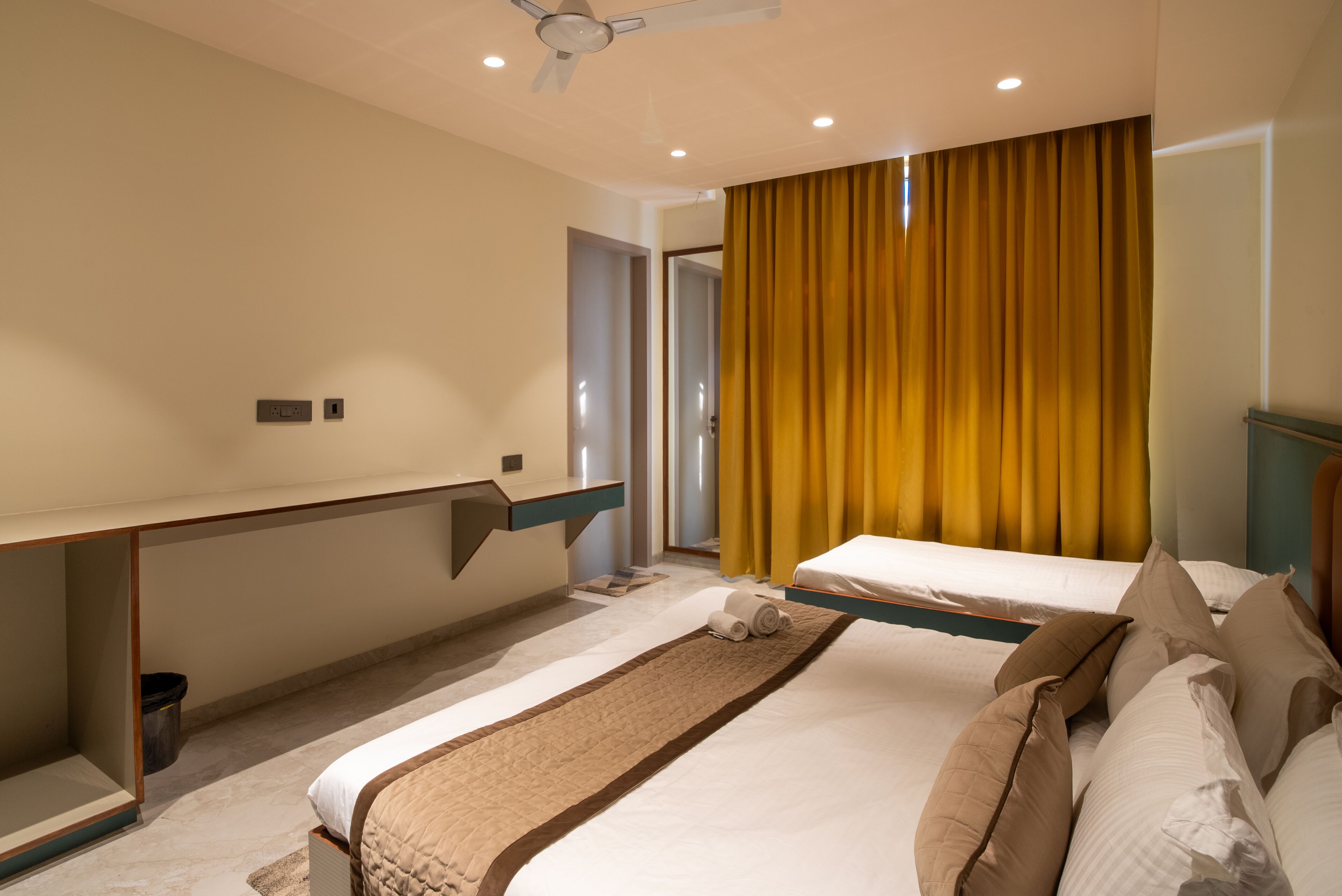 Ein Hotelzimmer mit einem Bett, einem Schreibtisch, einem Stuhl, einem Deckenventilator und einem Fenster mit Vorhängen.