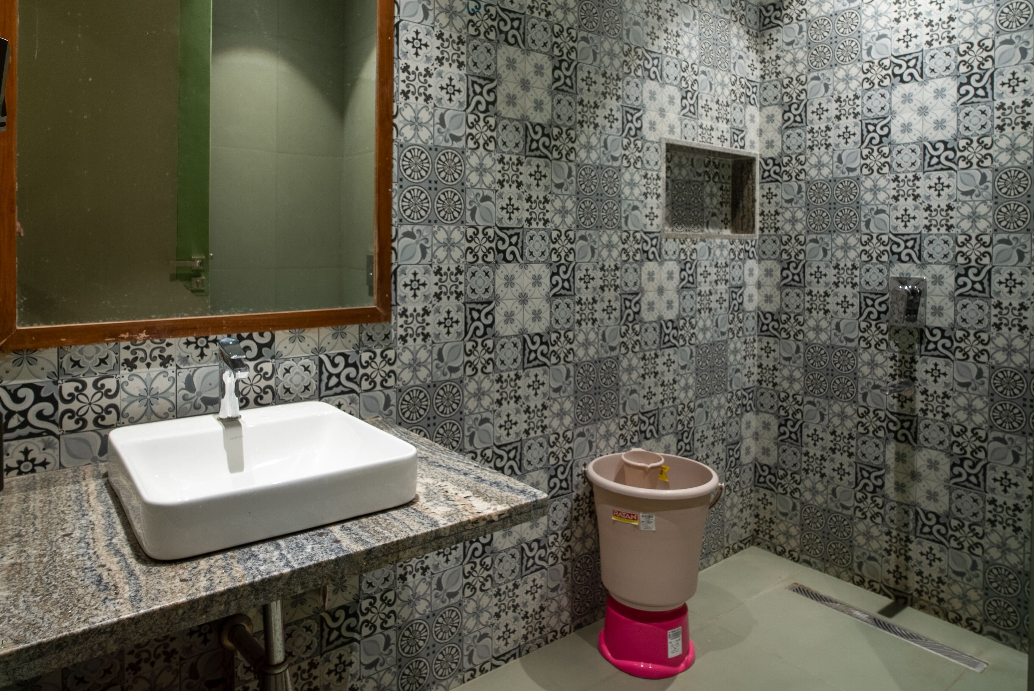 Une salle de bain avec des carreaux à motifs, un lavabo blanc et une poubelle rose.
