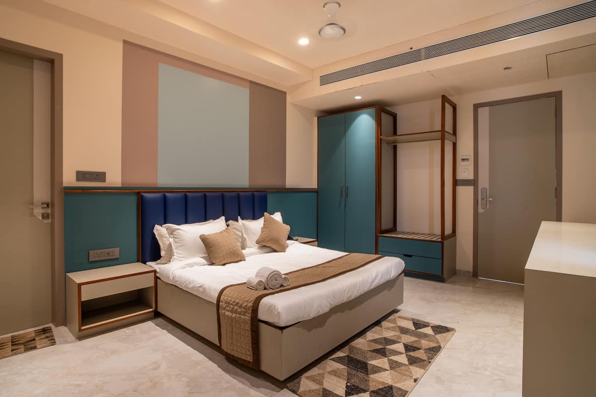 A modern hotel room with a large bed, a wardrobe, a seating area, and a bathroom.
