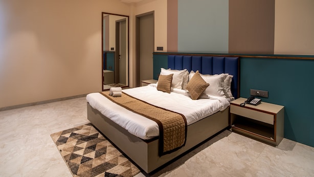 A modern hotel room with a large bed, a bedside table with a phone, and a mirror.
