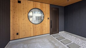 A modern interior with a wooden wall, a circular window, a door, and a concrete floor with stepping stones. - Hida machiyado KESHI (Takayama)
