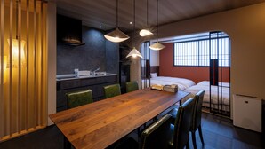 A modern hotel room with a wooden dining table, green chairs, a bed, a small kitchenette, and a window with bars. - Hida machiyado KESHI (Takayama)