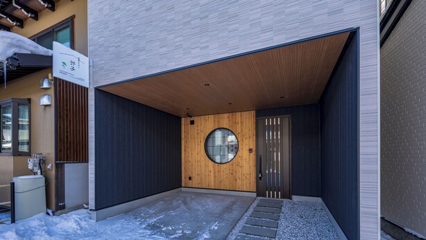 A modern building with a wooden door, a circular window, and a concrete pathway leading to the entrance. - Hida machiyado KESHI (Takayama)