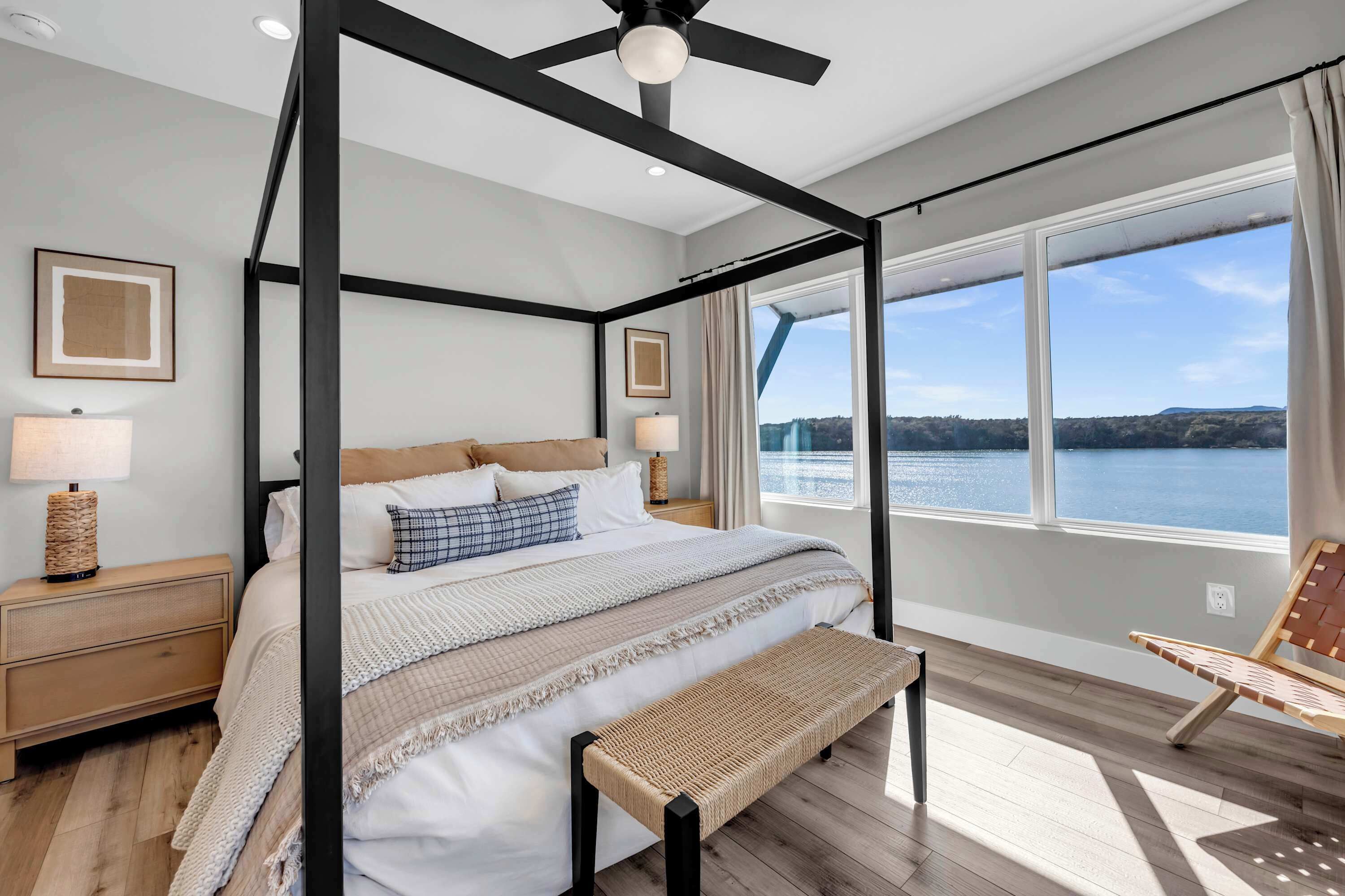 A four-poster bed with a view of a lake, a wooden bench, and a chair by the window.