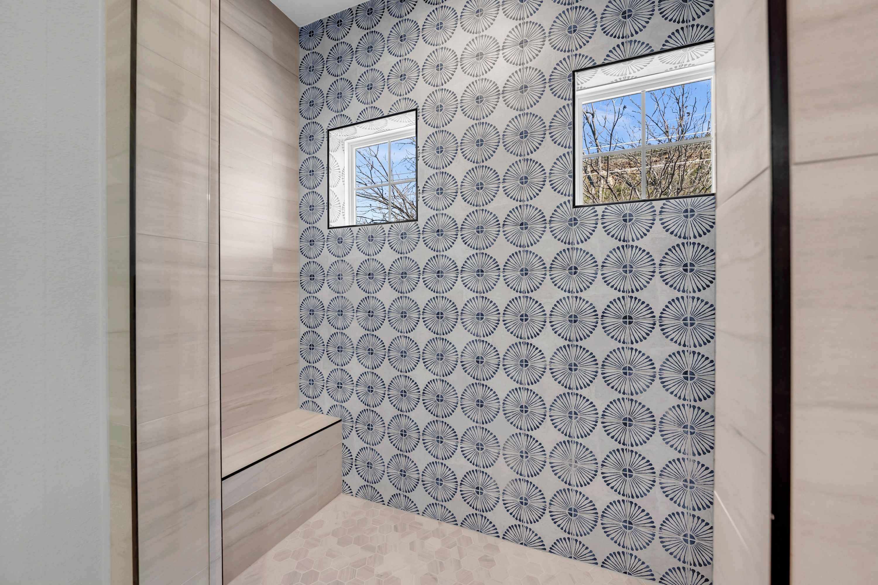 A bathroom with a patterned wall, two windows, and a tiled floor.