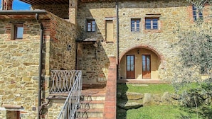 Ein Steinhaus mit einem zentralen Bogenportal, einem kleinen Balkon und einer Treppe zum Eingang.