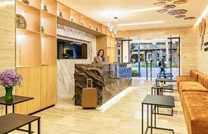 Welcome to our hotel lobby, featuring a reception desk, comfortable seating area, and a large window offering a view of the street.