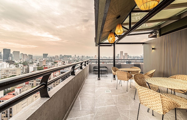 Relax on the rooftop with a panoramic city view from this elevated space, featuring a wicker seating area and a table.