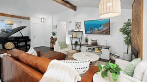 A living room with a piano, leather sofas, a round coffee table, and a large TV on the wall. - Stunning, Cozy, Private Backyard Lush Oasis with Pool! BBQ, 14 Mins to Disney (Santa Ana)