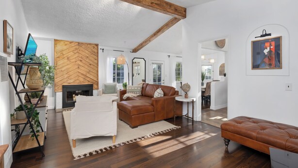 A spacious living room with a herringbone-patterned wall, a leather sofa, a white armchair, and a wooden bench. - Stunning, Cozy, Private Backyard Lush Oasis with Pool! BBQ, 14 Mins to Disney (Santa Ana)