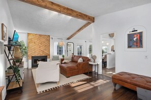 A spacious living room with a herringbone-patterned wall, a leather sofa, a white armchair, and a wooden bench. - Stunning, Cozy, Private Backyard Lush Oasis with Pool! BBQ, 14 Mins to Disney (Santa Ana)