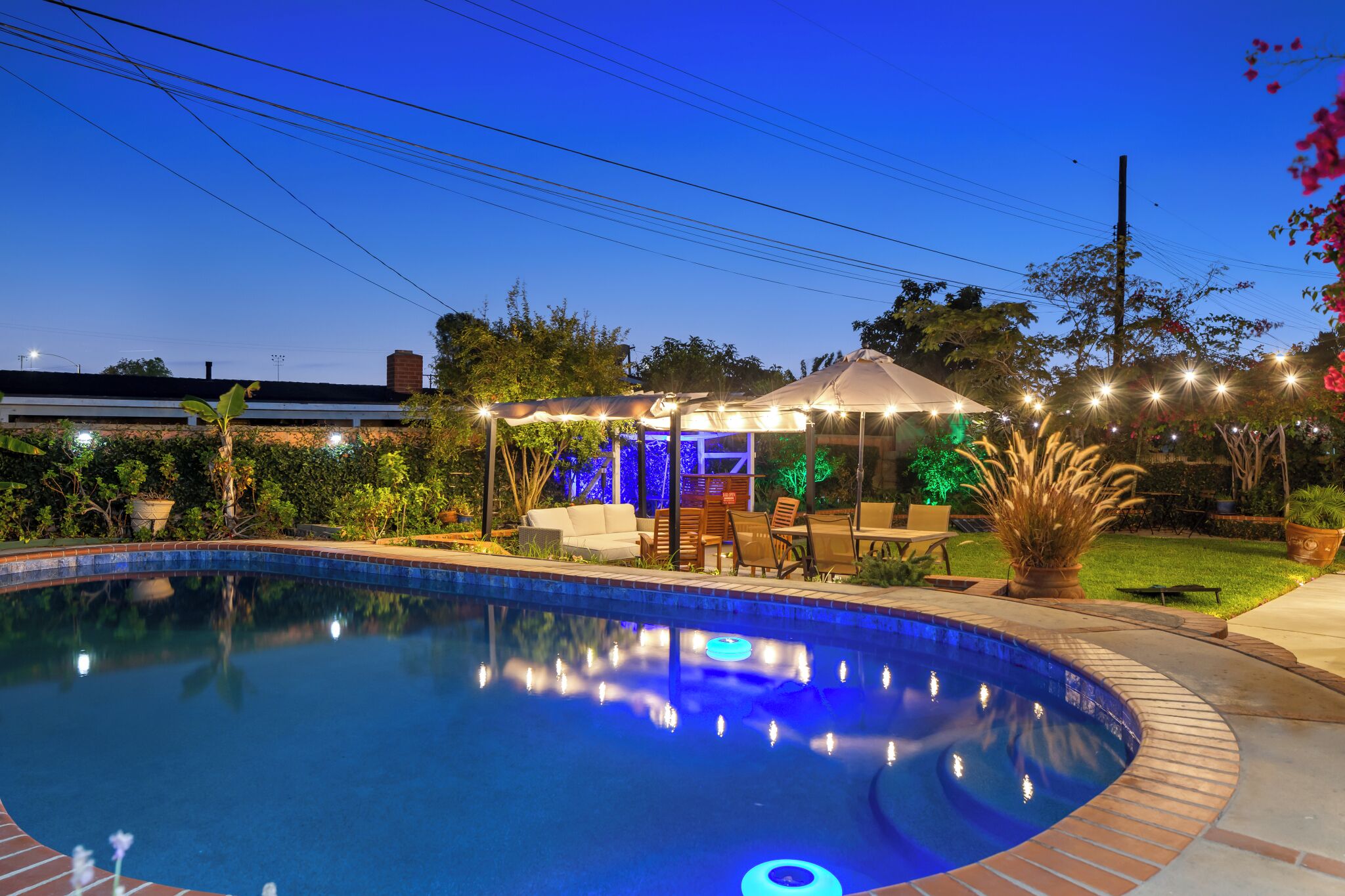 A swimming pool with a patio area, surrounded by plants and a gazebo.