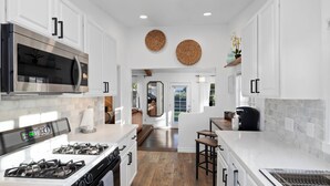 A modern kitchen with white cabinetry, stainless steel appliances, and a central island with stools. - Stunning, Cozy, Private Backyard Lush Oasis with Pool! BBQ, 14 Mins to Disney (Santa Ana)