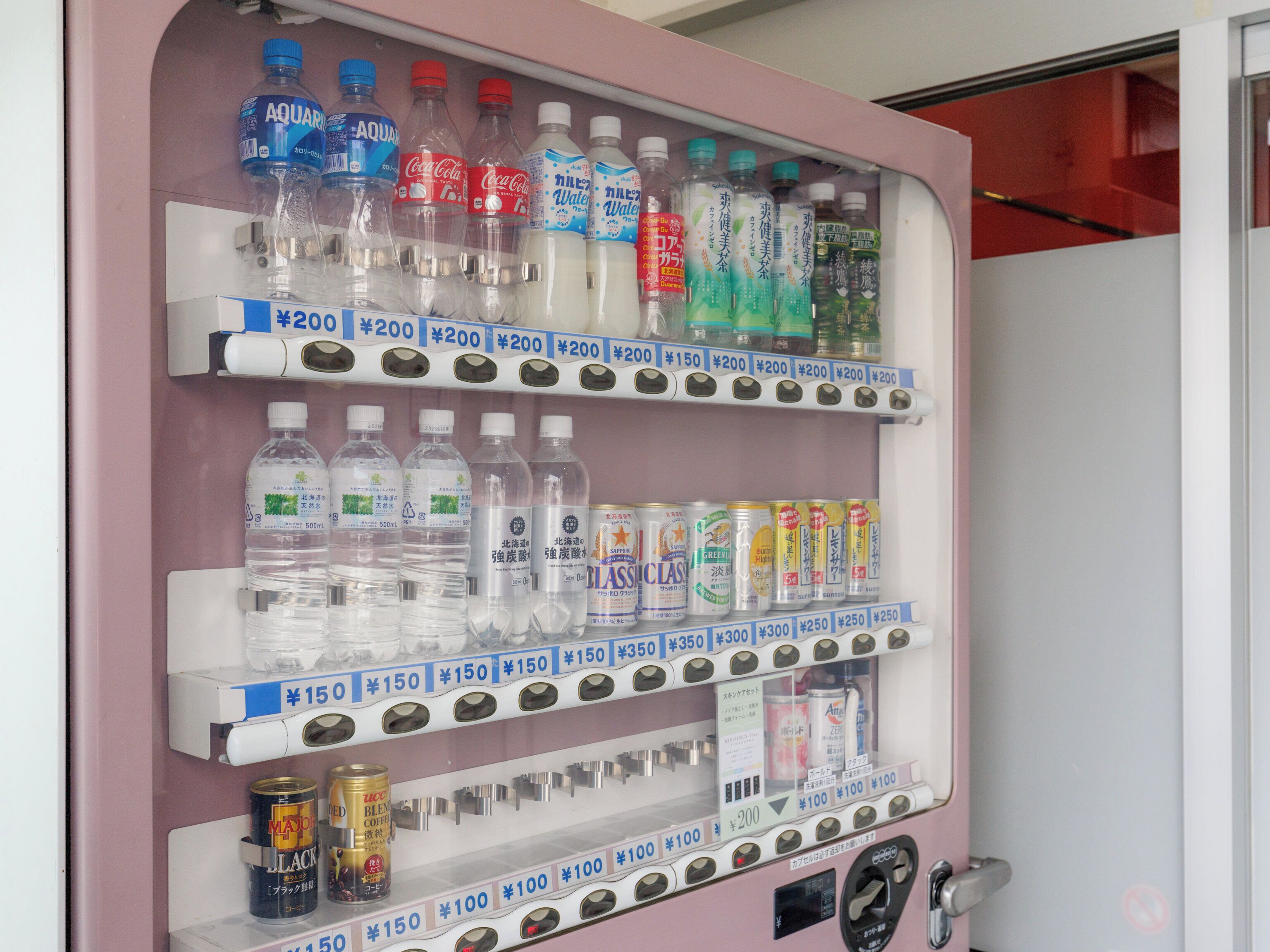 A vending machine with various beverages and snacks, including water, soda, and canned drinks, with price labels in Japanese.