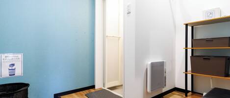 Habitación de hotel con pared azul, suelo de madera, un cubo de basura negro, un banco negro y un estante con cajas de almacenamiento.