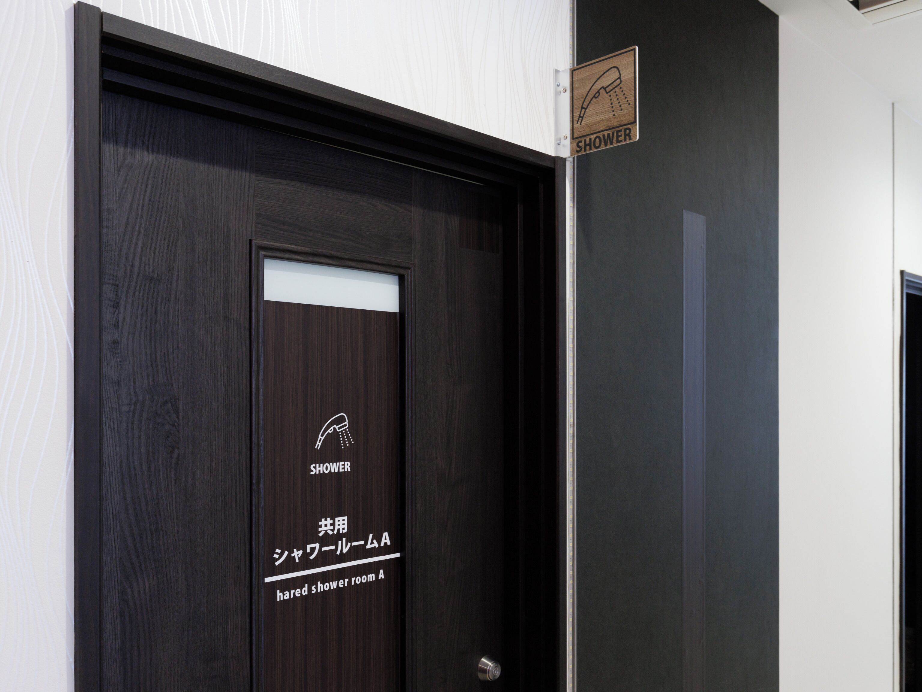 Une porte en bois sombre, sur laquelle on peut voir un panneau indiquant la présence d’une douche, ainsi qu’une étiquette précisant qu’il s’agit d’une salle de douche à usage collectif.