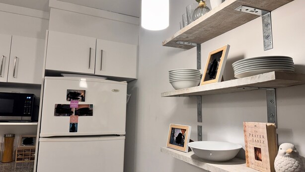 Een keuken met witte kasten, een ingebouwde magnetron en planken met servies, een boek en een decoratief vogeltje.