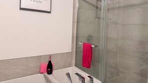 Een moderne badkamer met een glazen douchecabine, een lijst met een citaat aan de muur en een fles champagne op het aanrecht.
