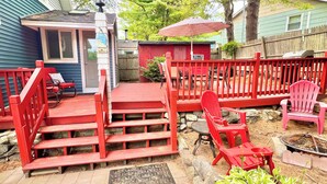 Una terraza roja con escalones que conducen a un espacio cubierto, rodeada por una cerca de madera y diversas opciones de asientos.