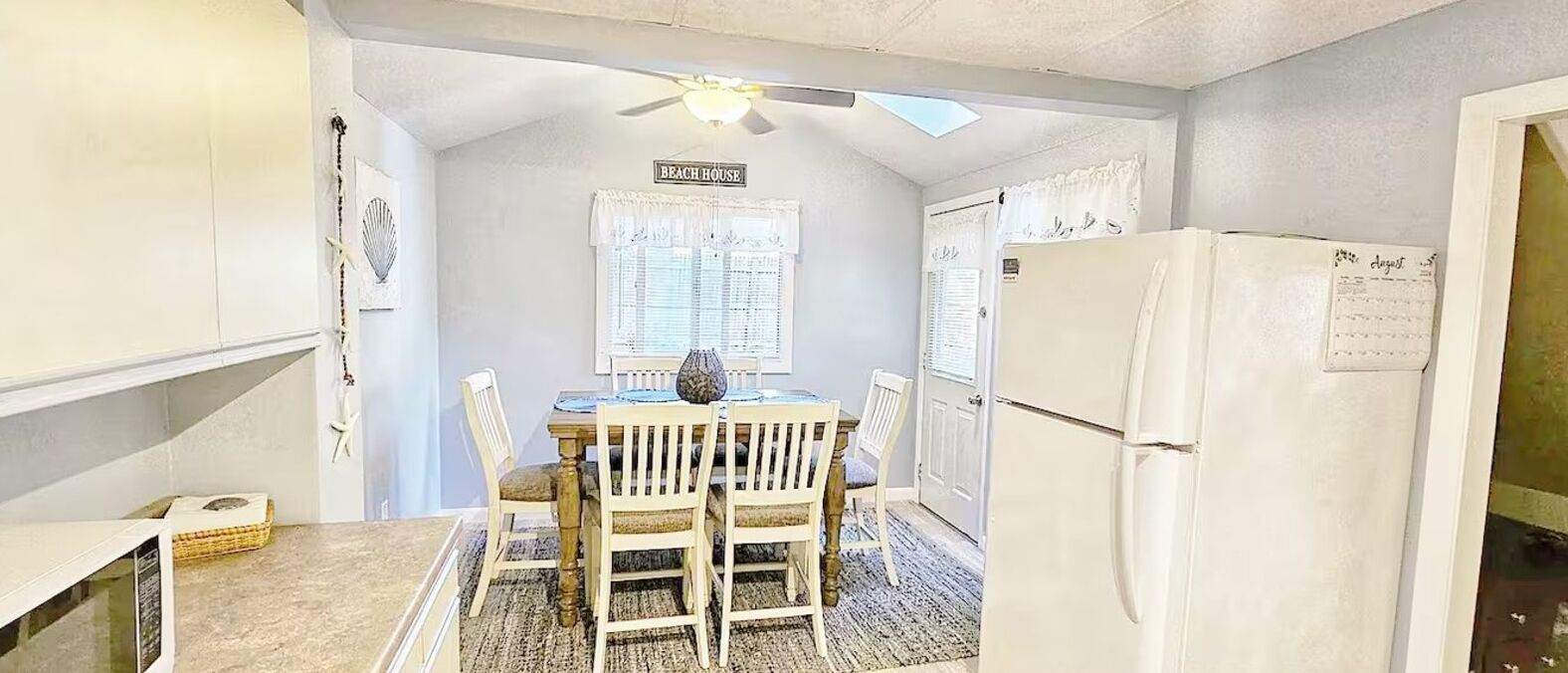 A compact kitchen with a dining table, chairs, a ceiling fan, and a refrigerator.
