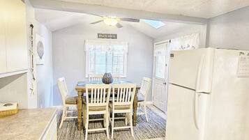 A compact kitchen with a dining table, chairs, a ceiling fan, and a refrigerator.