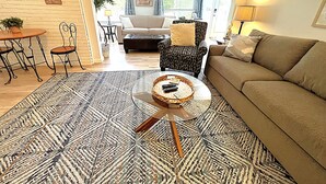 Una sala de estar con un tapete estampado, una mesa de centro redonda con una cesta, un sofá, un sillón estampado y una zona de comedor con mesa y sillas.