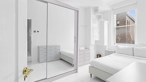 Une chambre moderne avec une grande armoire, un lit, une table de chevet et une fenêtre donnant sur un immeuble en briques.