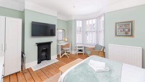A bedroom with a bed, a desk, a chair, a fireplace, a radiator, a TV, and a window with blinds. - Traditional Bath House, Garden with City Views (Bath and North East Somerset)