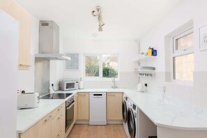 A modern kitchen with a dishwasher, microwave, and toaster. There is a window with a view of trees and a sink with a faucet. - Traditional Bath House, Garden with City Views (Bath and North East Somerset)