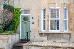 A stone building with a green door, a window with shutters, and a small garden area. - Traditional Bath House, Garden with City Views (Bath and North East Somerset)