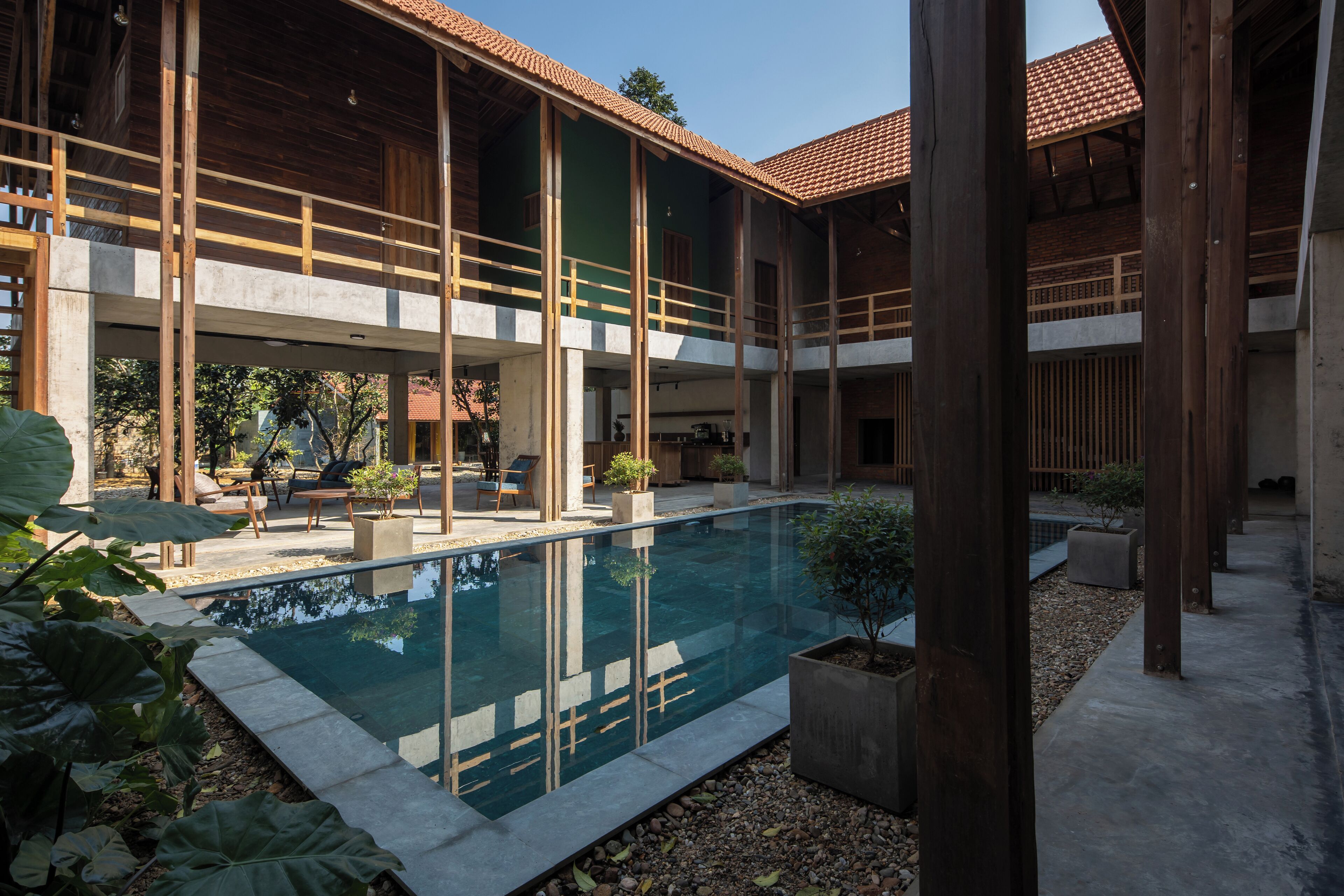 Un bâtiment moderne doté d’une piscine, de poutres en bois et d’un espace extérieur aménagé pour s’asseoir.