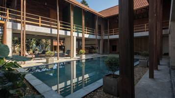 Un bâtiment moderne doté d’une piscine, de poutres en bois et d’un espace extérieur aménagé pour s’asseoir.