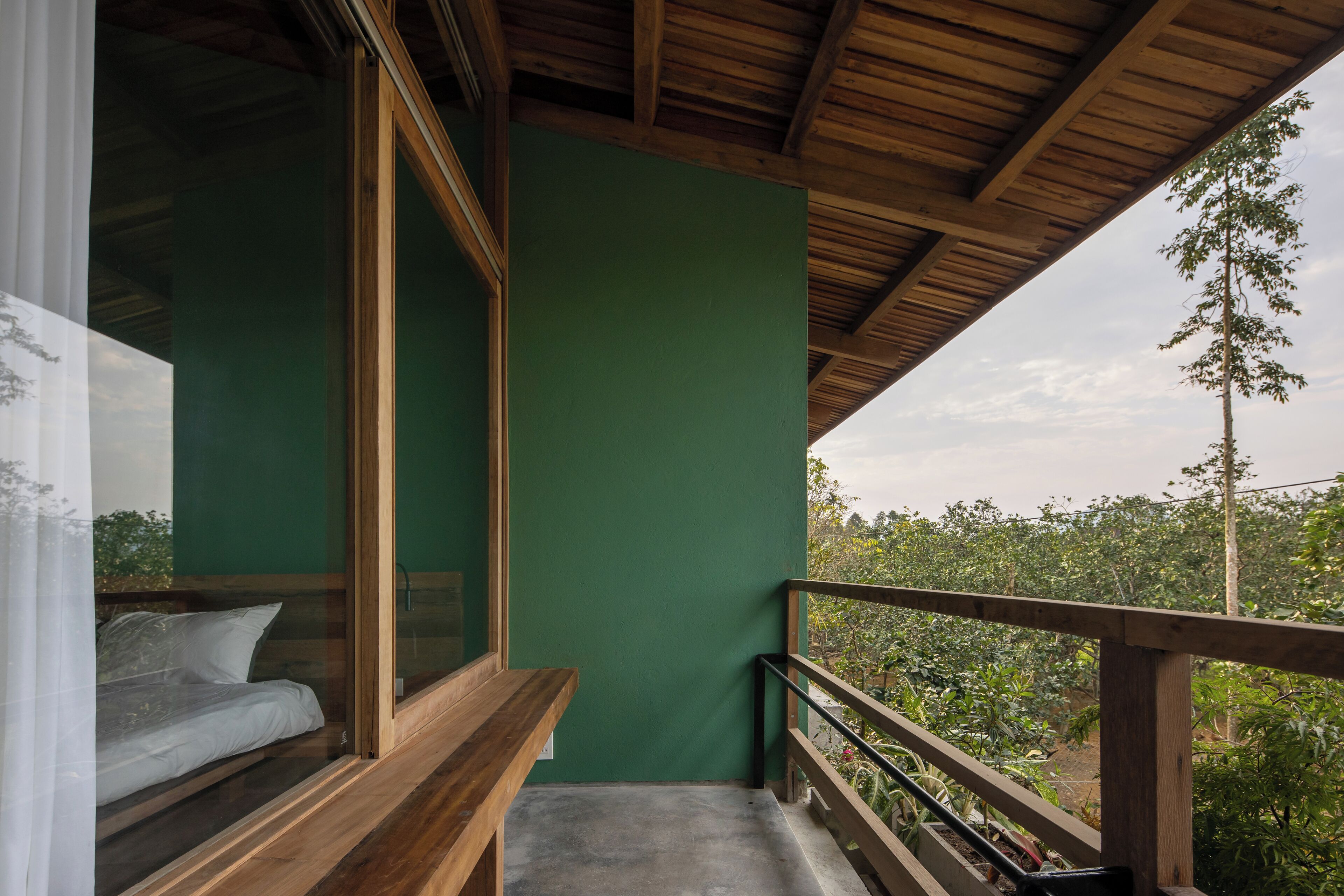 A balcony with a wooden railing, a green wall, and a bed with white bedding.