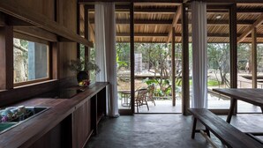 A modern kitchen with wooden cabinets, a sink, and a window overlooking a patio area with outdoor furniture. - Hachi Homestay & Spa (Hue)