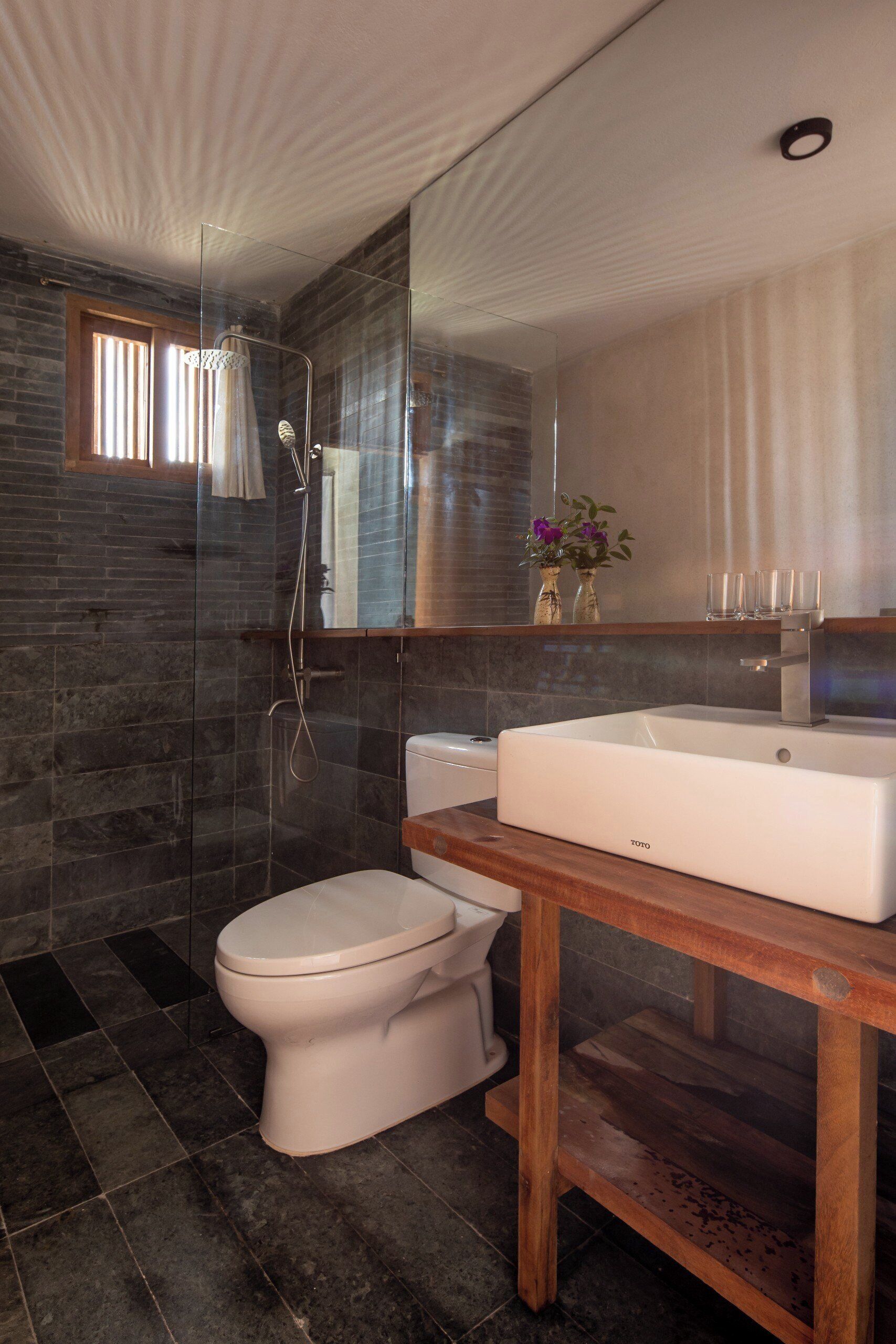 A modern bathroom with a glass-enclosed shower, a white toilet, and a wooden vanity with a large sink.