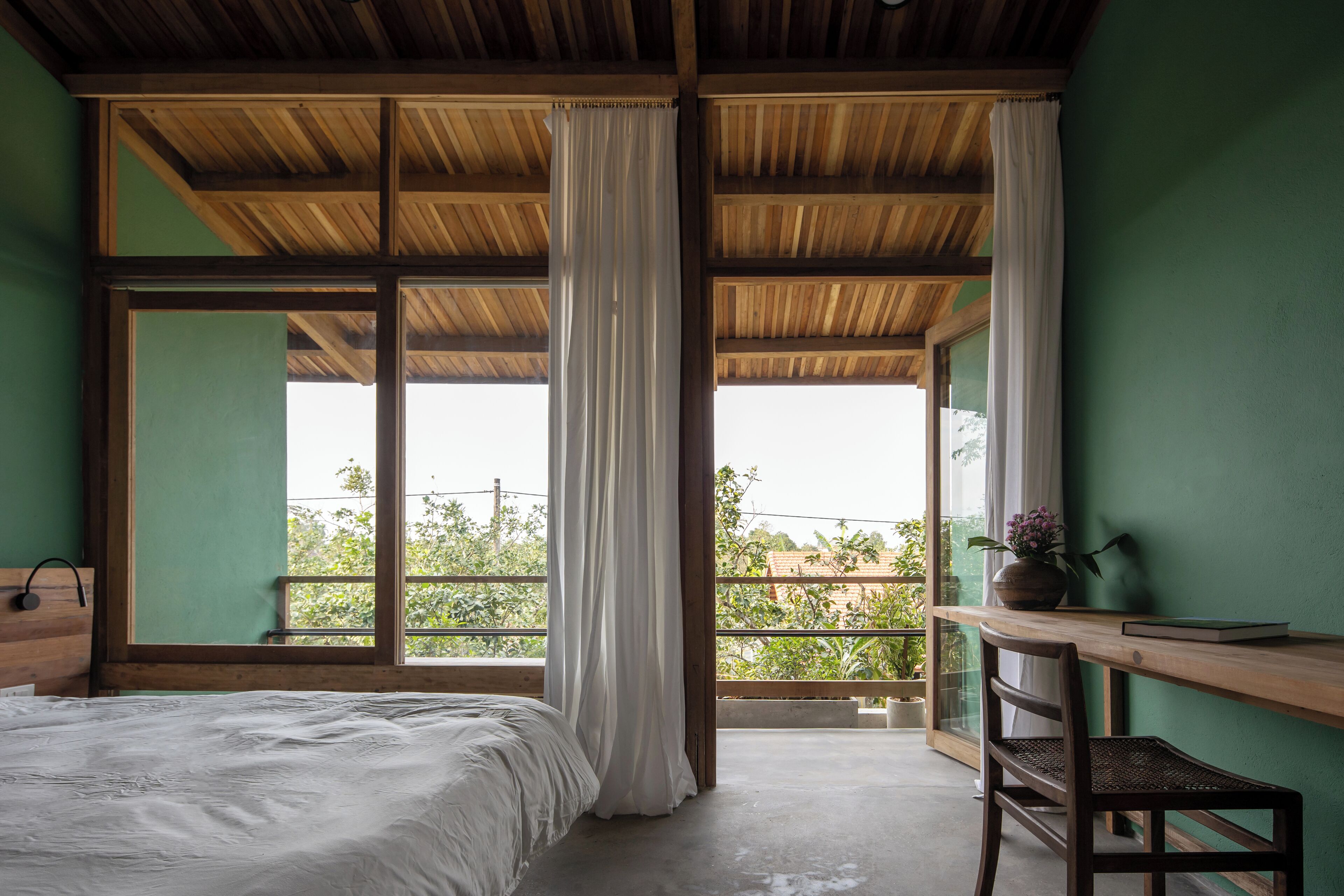 Ein Schlafzimmer mit großem Fenster, einem Bett, einem Holztisch und einem Sessel.