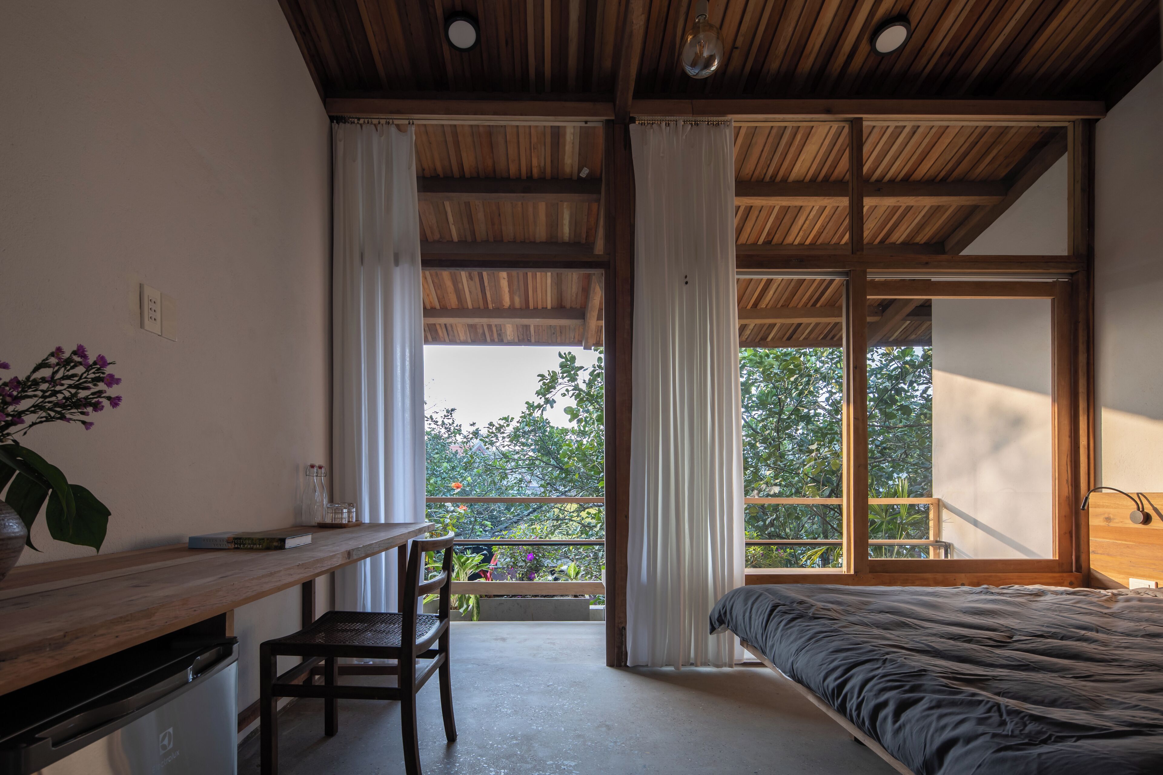 Un dormitorio con un ventanal grande, una cama, un escritorio y una silla.
