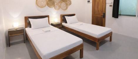 A room with two wooden beds, a wall-mounted decorative basket, a wooden door, and a window with curtains.