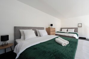Two single beds with grey headboards and white bedding, complemented by a wooden nightstand and black lamp.