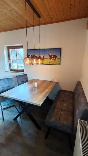 Enjoy meals in this dining area with a wooden table and benches, a large window offering a view of the outside, and a beautiful painting above.