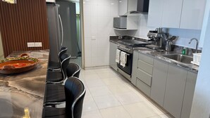 Una cocina moderna con horno empotrado, un lavamanos de acero inoxidable y un comedor con encimera de mármol y sillas negras.