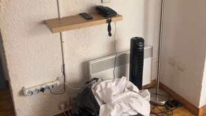 Een kamer met een wandgemonteerde televisie, een telefoon, een verwarming en een afvalbak.